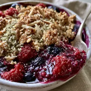 Extreme close-up of Breakfast Crumble showing bubbling blueberries, red raspberries, and golden-brown toasted oat clusters with hemp seeds.